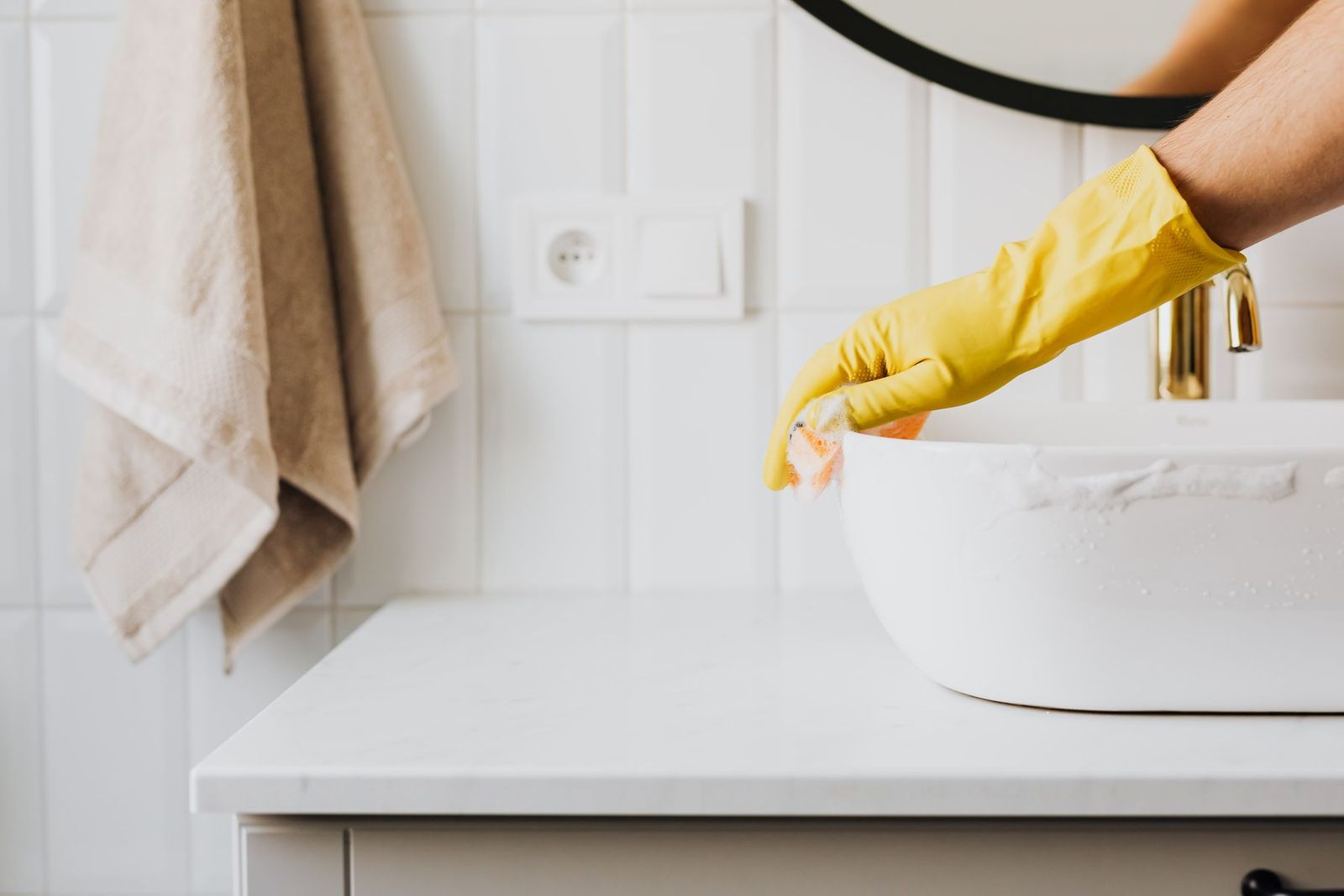 Waschbecken im Bad wird mit gelben Handschuhen gereinigt